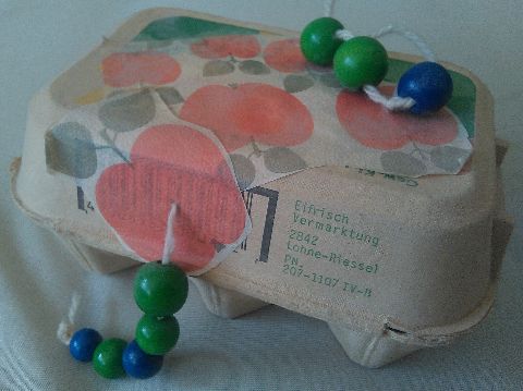 Wurm aus Perlen an einer mit Äpfeln beklebten Eierschachtel