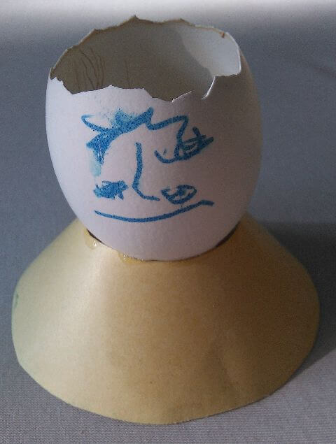 Aufgeschlagene Eierschale mit aufgemaltem Gesicht auf einem Pappring