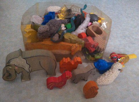 eine Kiste mit vielen Spielzeugtieren, davor einige ausgewählte: ein großer Elefant, ein Kamel, ein Hahn, ein Esel und ein Affe, sowie ein blauer Gummilöwe, ein gestrickter weißer Vogel und ein Metallvogel zum Aufziehen