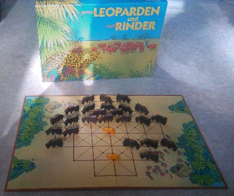Schachtel und Spielplan mit vielen Holzrindern und zwei Leoparden