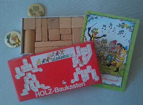Holzbausteine in einem Kasten, dazu zwei Lurchi-Ansteckbuttons und eine Karte