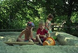 Ich sitze neben anderen Kindern in einem Sandkasten