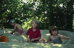 Ich sitze neben anderen Kindern in einem Sandkasten